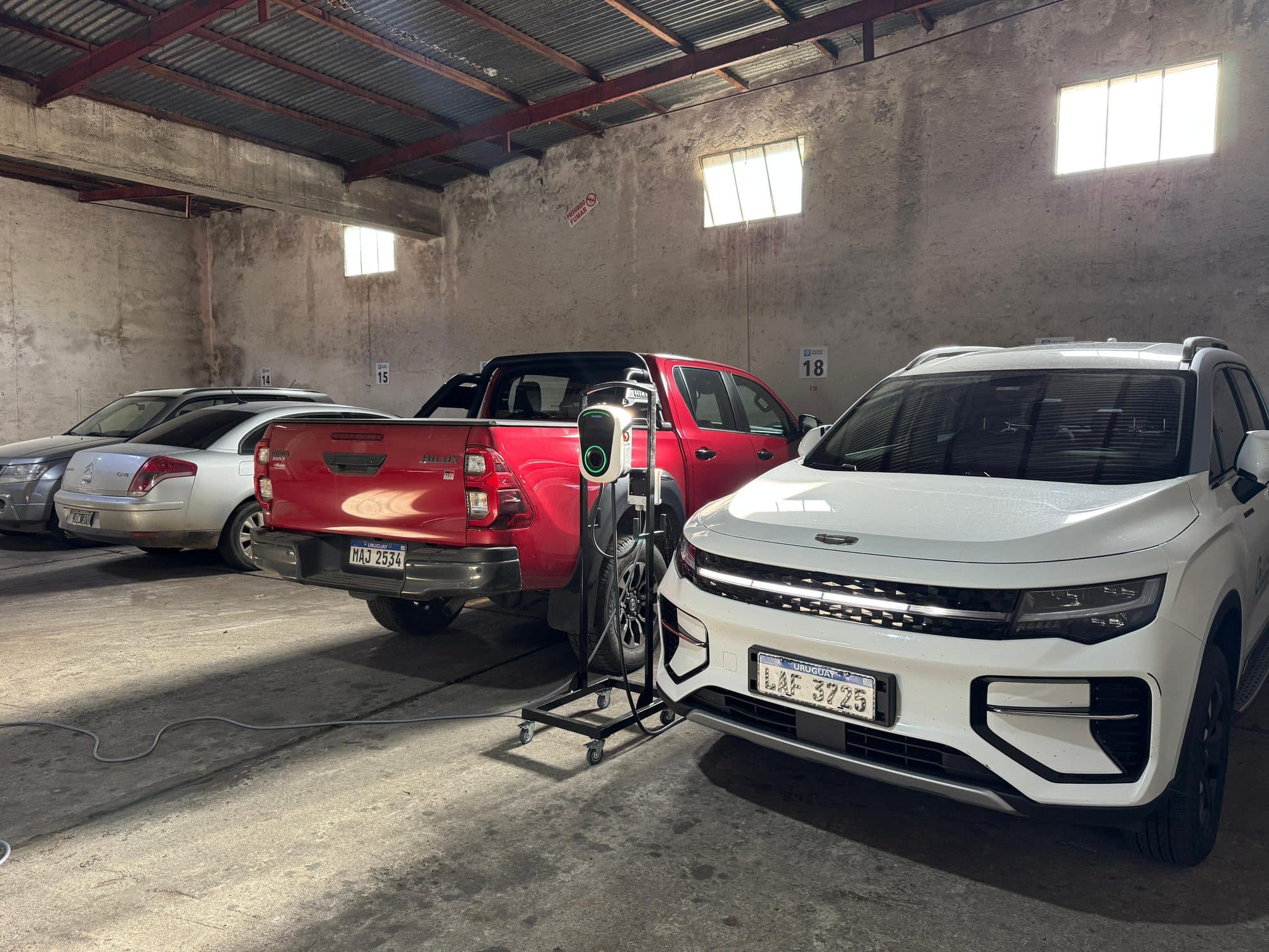 Cargador para autos eléctricos con conector tipo 2 junto a una camioneta en el estacionamiento